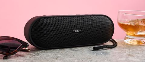 Tribit XSound Plus 2 on gray surface with pair of sunglasses to its left and a half-filled glass with ice to its right