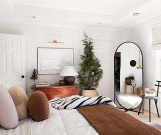 White bedroom, black framed mirror, tree in basket