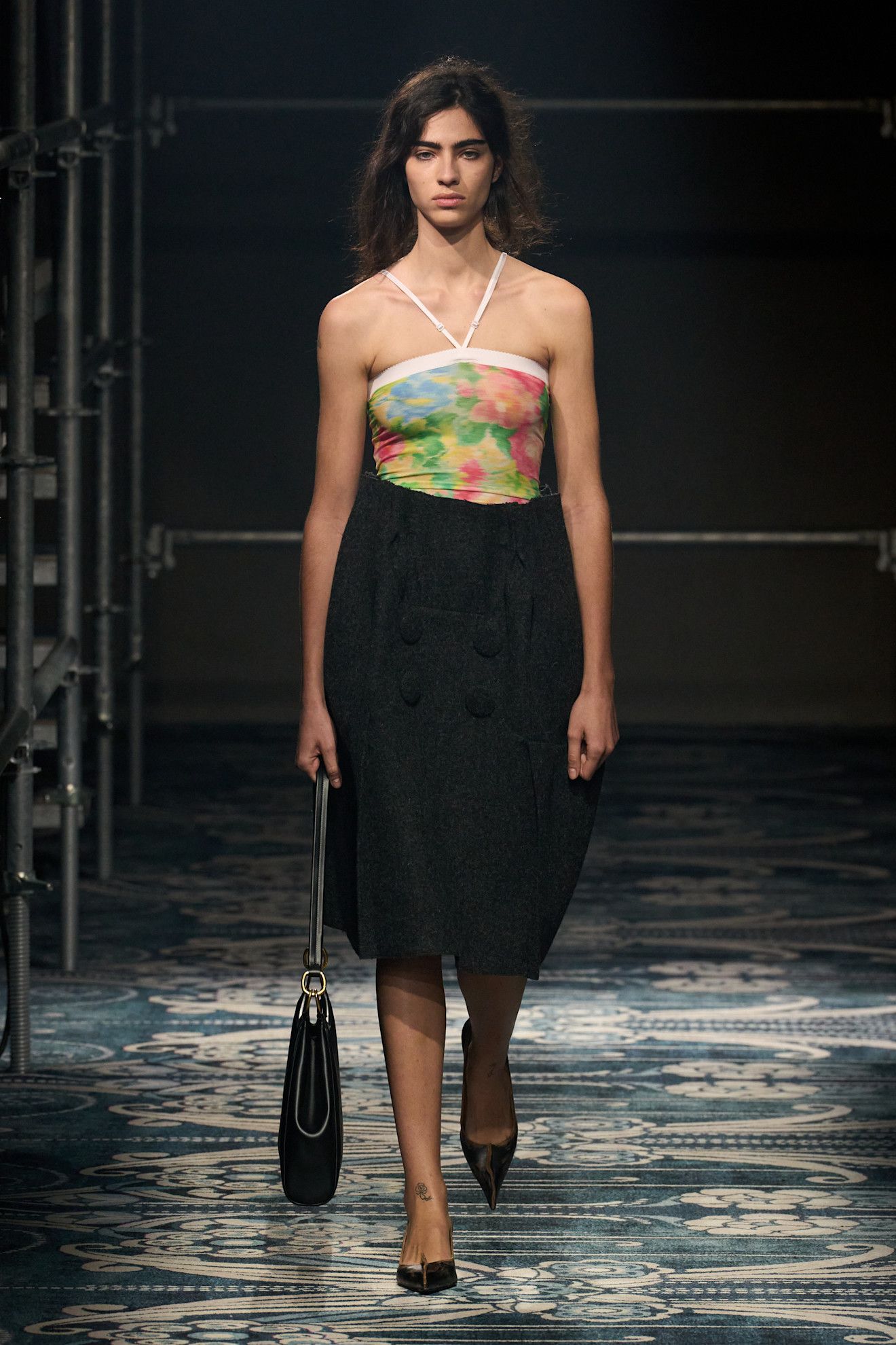 A F/W 25 Prada model wearing a floral halter bodysuit and a tailored midi skirt with pumps.
