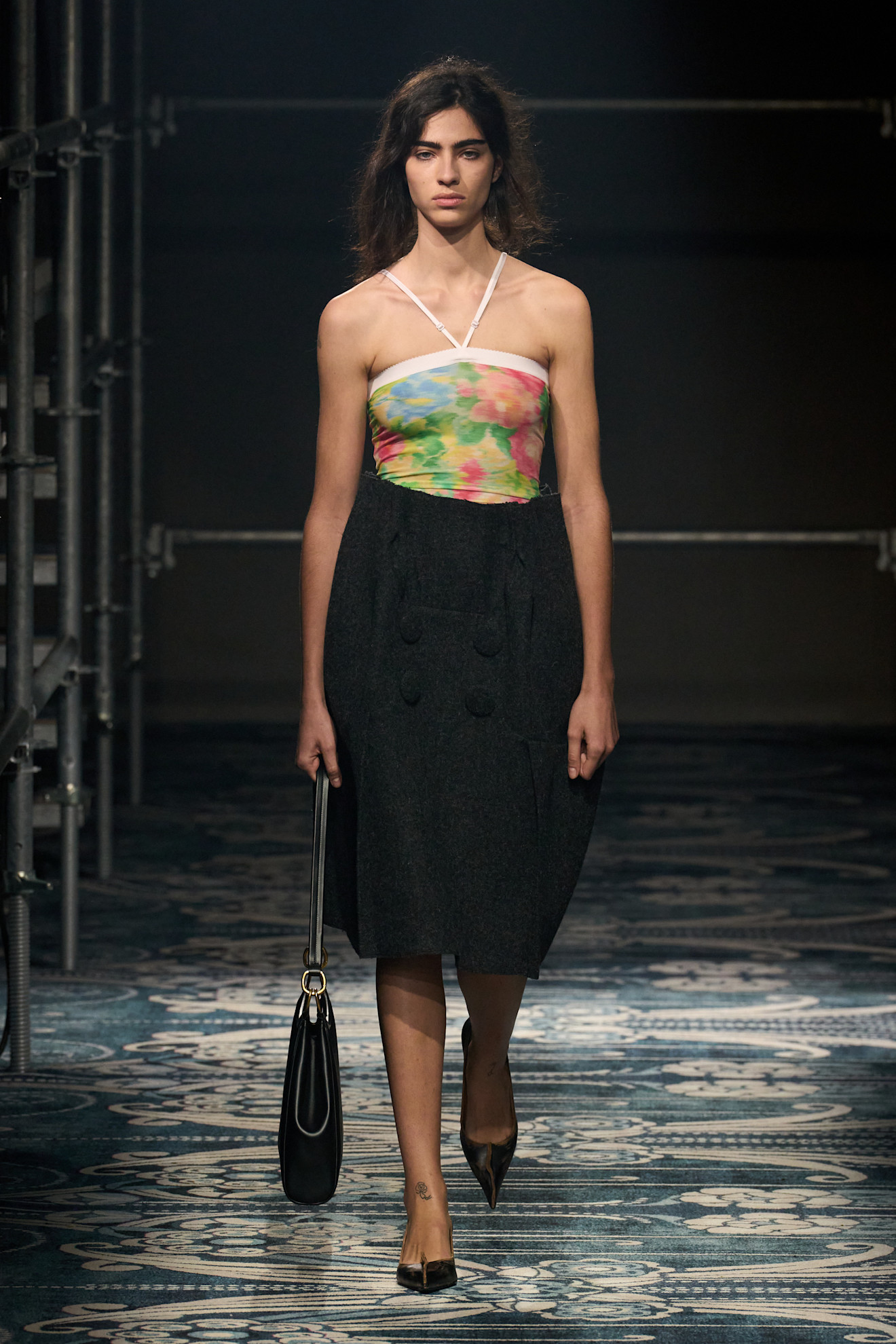 A F/W 25 Prada model wearing a floral halter bodysuit and a tailored midi skirt with pumps.