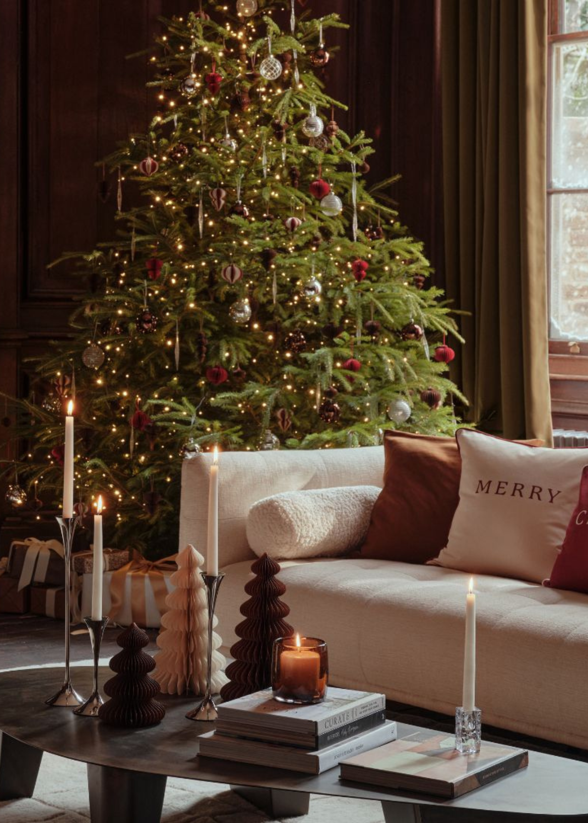 A living room decorated for Christmas with a tree, embroidered pillows, paper ornaments, and candles
