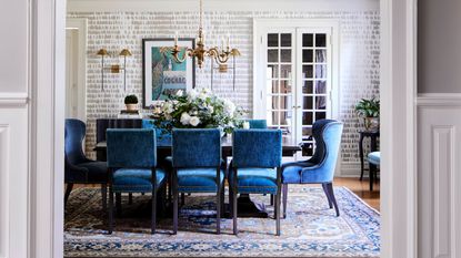 Dining room with large dining table, blue velvet dining chairs, a gray and white wallpaper and Persian style rug