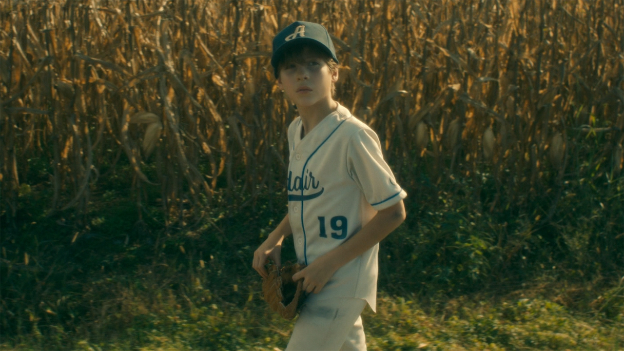 Jacob Tremblay stands in front of a corn field, in his baseball uniform, in Doctor Sleep.