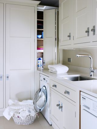 Contemporary style utility room design with cream shaker style units, wicker laundry basket and a washing machine and tumble dryer