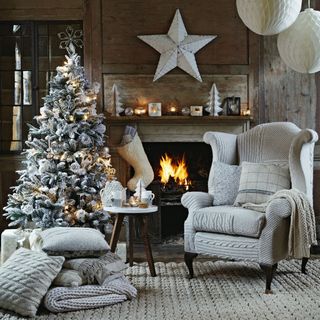 Frosted Christmas tree decorated with baubles inside furnished grey living room with fireplace