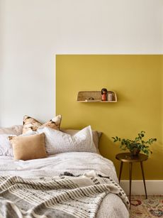 Yellow painted wall behind bed with wall light and soft furnishings