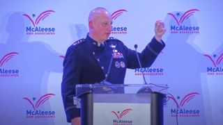 A man in uniform holds up his bend arm behind a podium.