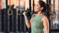 Woman in green vest doing a dumbbell curl in a gym