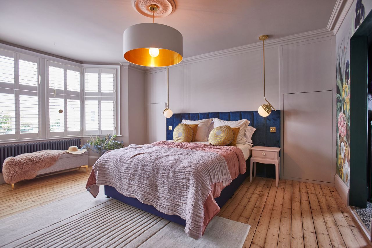 The bottom floor bedroom shows a large window looking onto the front small garden and pink sheets with wooden flooring