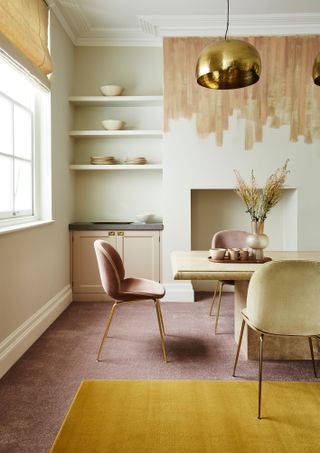 Fabric chairs in neutral colored dining space with hand painted mantle space and yellow ochre rug over dusk pink carpet