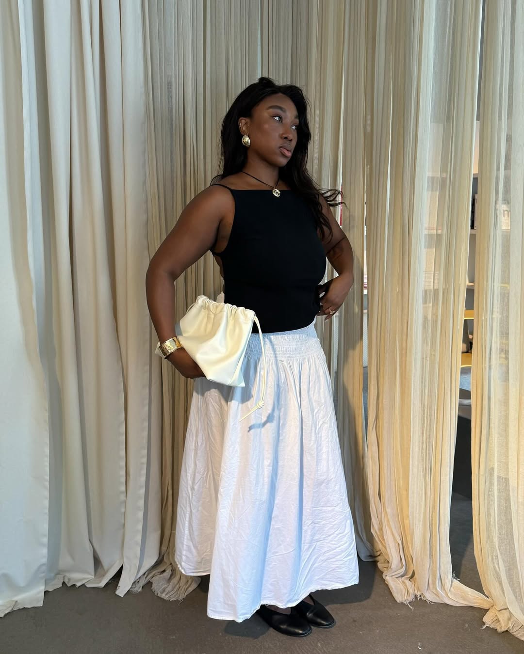 @nnennaechem wears a white poplin skirt, black boat neck tank top, black ballet flats and a pale yellow ruched clutch bag