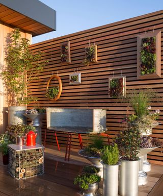 Balcony garden with decking, recycled furniture and containers filled with succulents and herbs hanging on the wall, insect hotel coffee table, trailing house plants