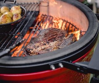 BBQ grill with flames cooking meat and potatoes