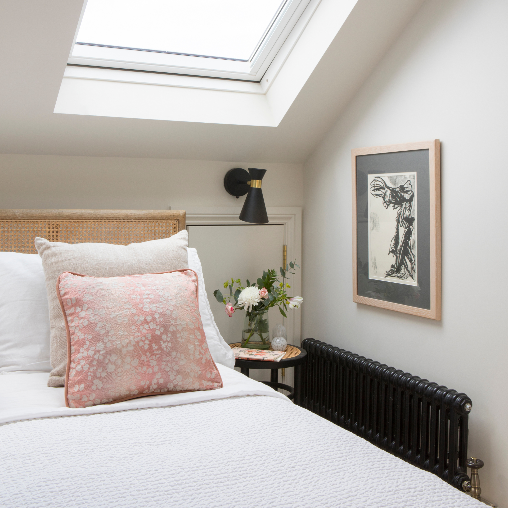 White bedding on a double bed. There is a pink floral decorative pillow and large skylight above.