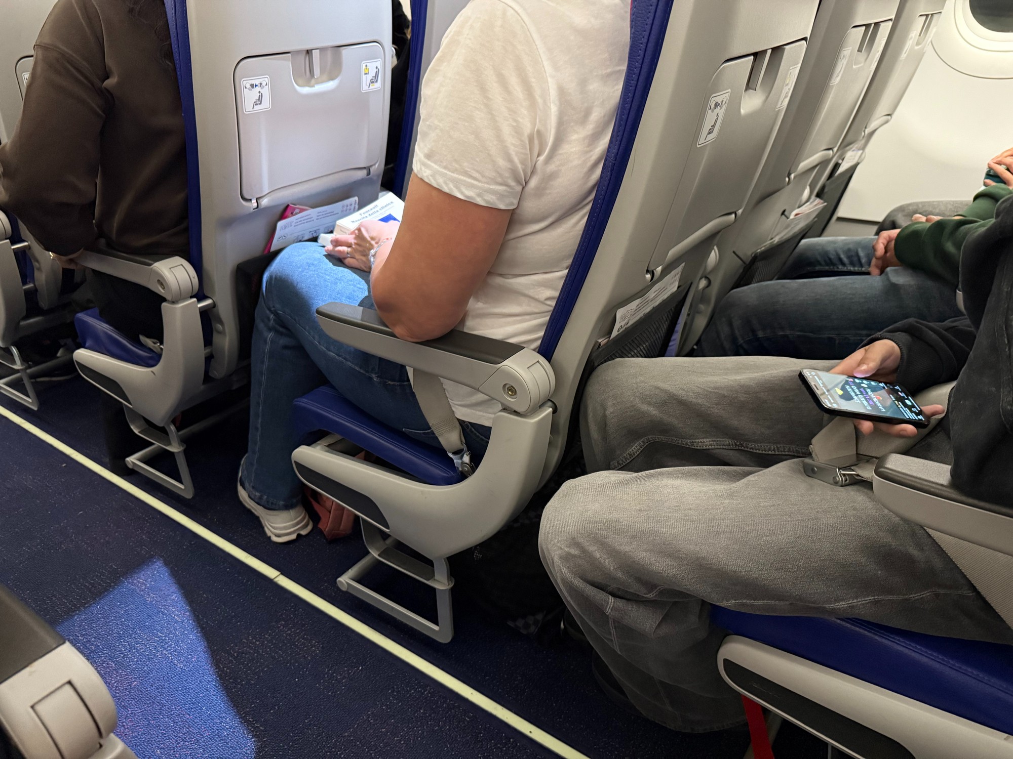 Passengers seated inside an airplane cabin with visible seat belts, legroom, and personal belongings during a commercial flight