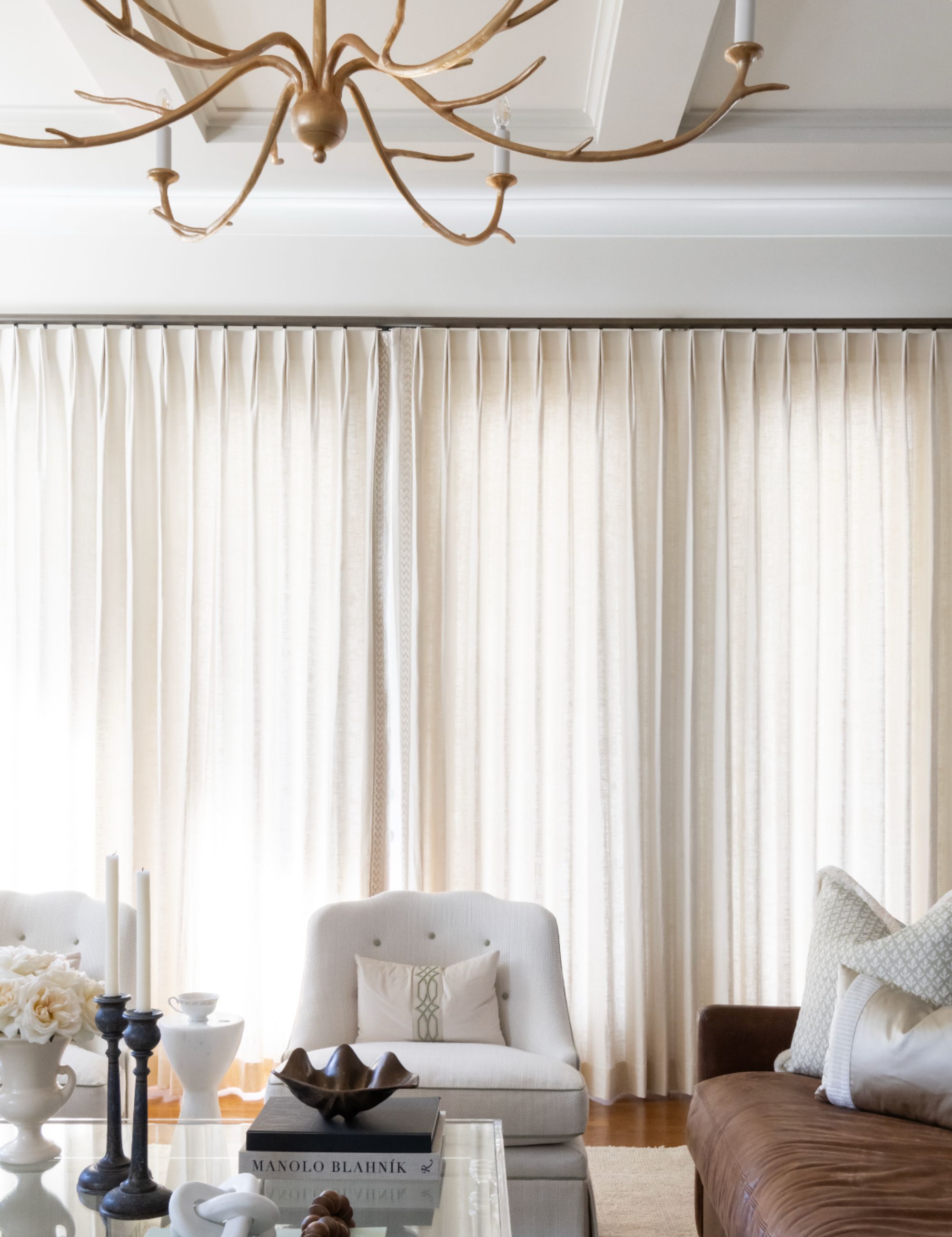 Neutral colored room with white armchair, tan sofa and white drapery and curtains