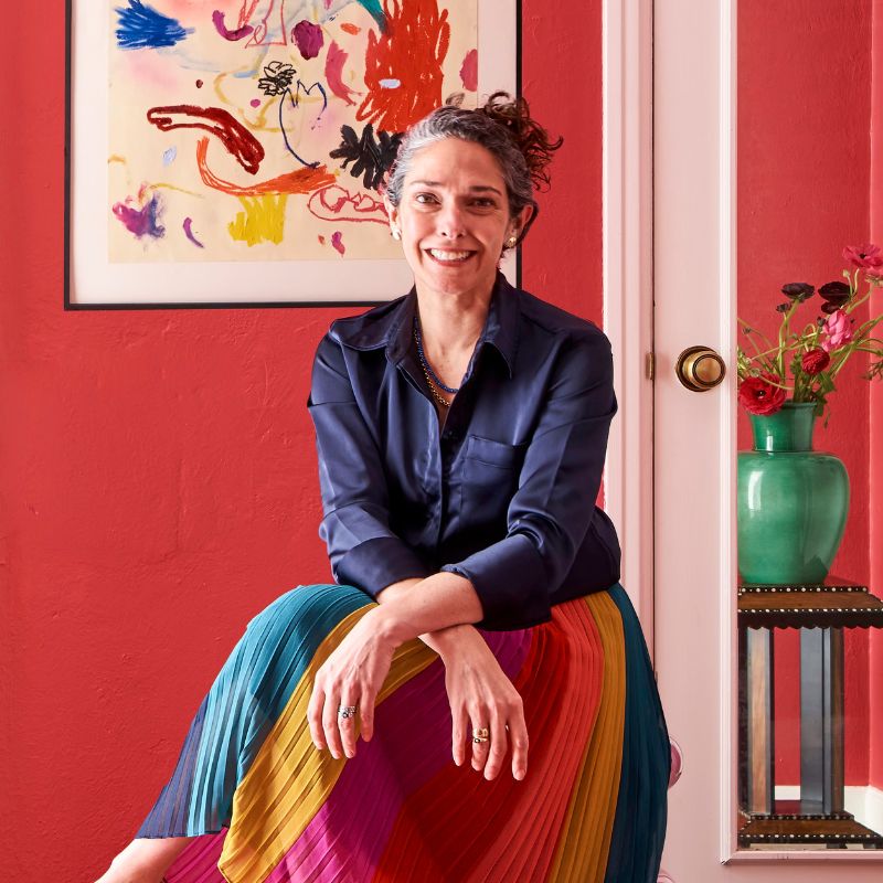  Nadia Watts in multi-colored skirt in front of bright red wall with abstract artwork