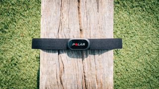 A black Polar H10 heart rate monitor wrapped around a wooden bench, with the focus on the main part of the strap