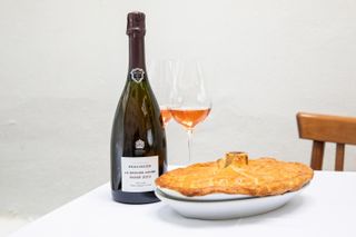 Bottle of Bollinger La Grande Année 2012 next to 2 glasses and a baked pie in a white plate
