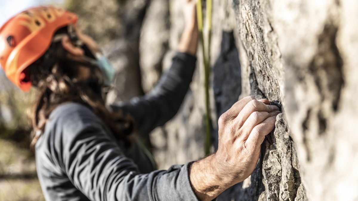 A man rock climbing wearing an orange helmet