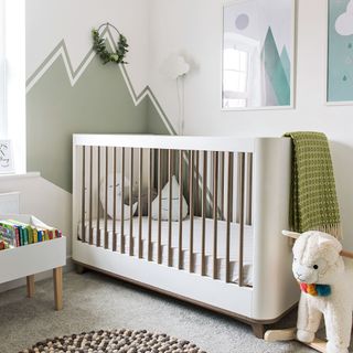 Simple nursery with smart white cot and a mountain mural painted in sage green