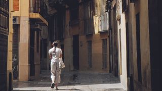 woman walking through sunlit street with dark shadows