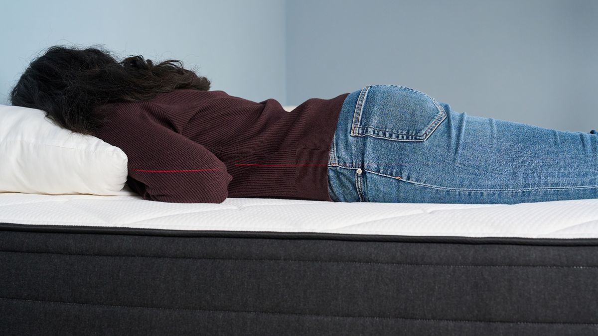 Mattress tester Becky George lies on her stomach on the surface of the Plank Firm Luxe mattress. A laser line can be seen going across the body, indicating that her spine is held in a straight line