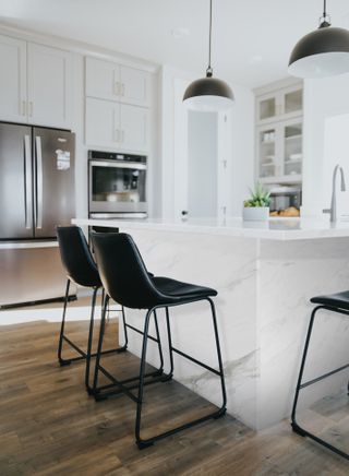 white kitchen with island, breakfast bar, black bar stools and pendants