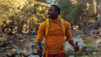 A cheerful African American hiker is standing next to a mountain stream in the forest