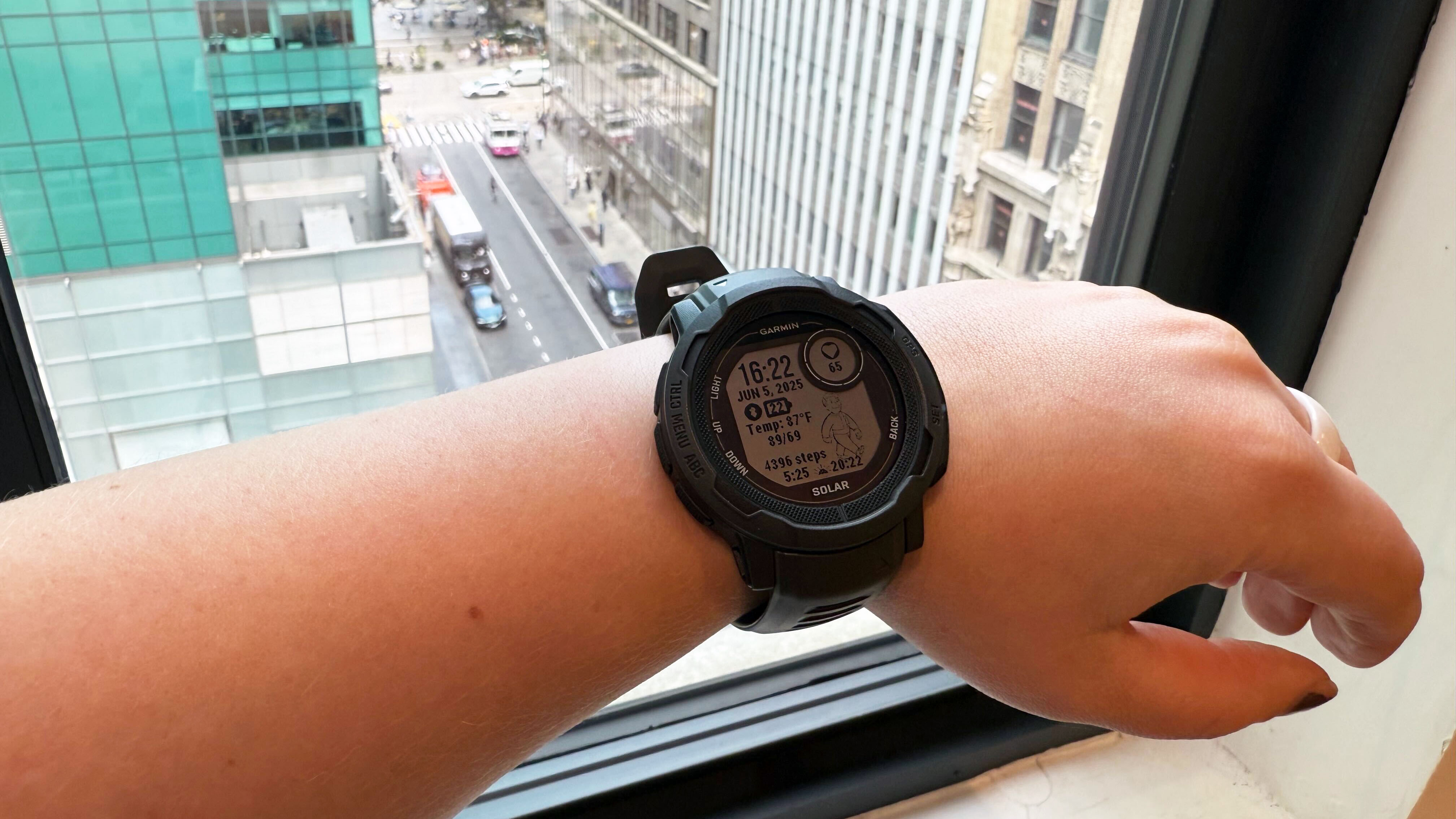 Garmin Instinct 2 Solar on left wrist, in front of a window overlooking Bryant Park in New York City.