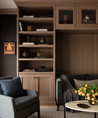 A moody home office with built-in wooden shelving and a small dark gray sofa