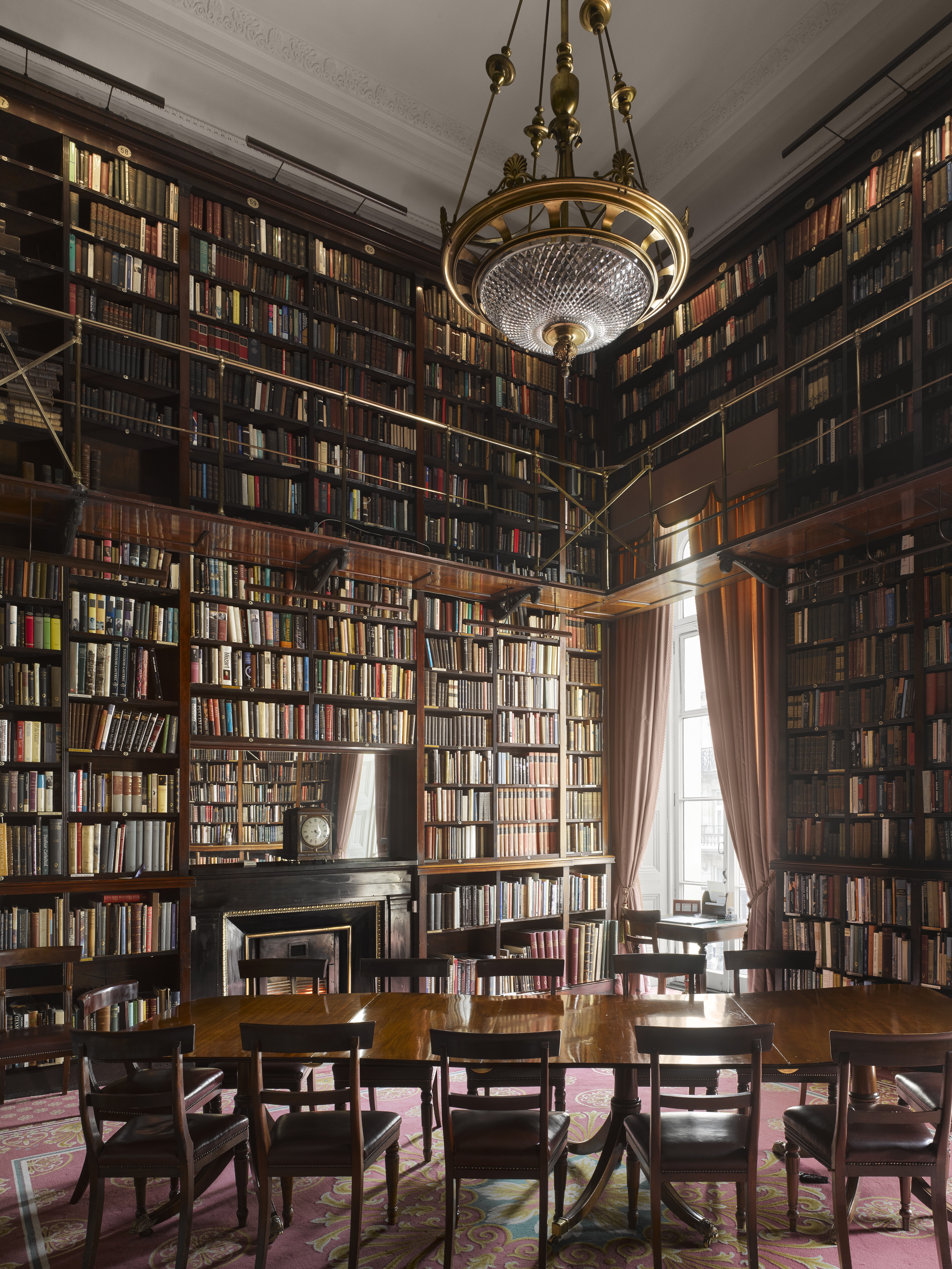 Double height library shelves, a wooden table and leather chairs