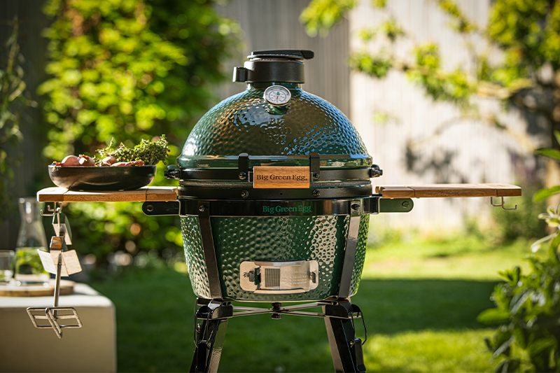 Big Green Egg MiniMAx in garden on stand in promotional image 