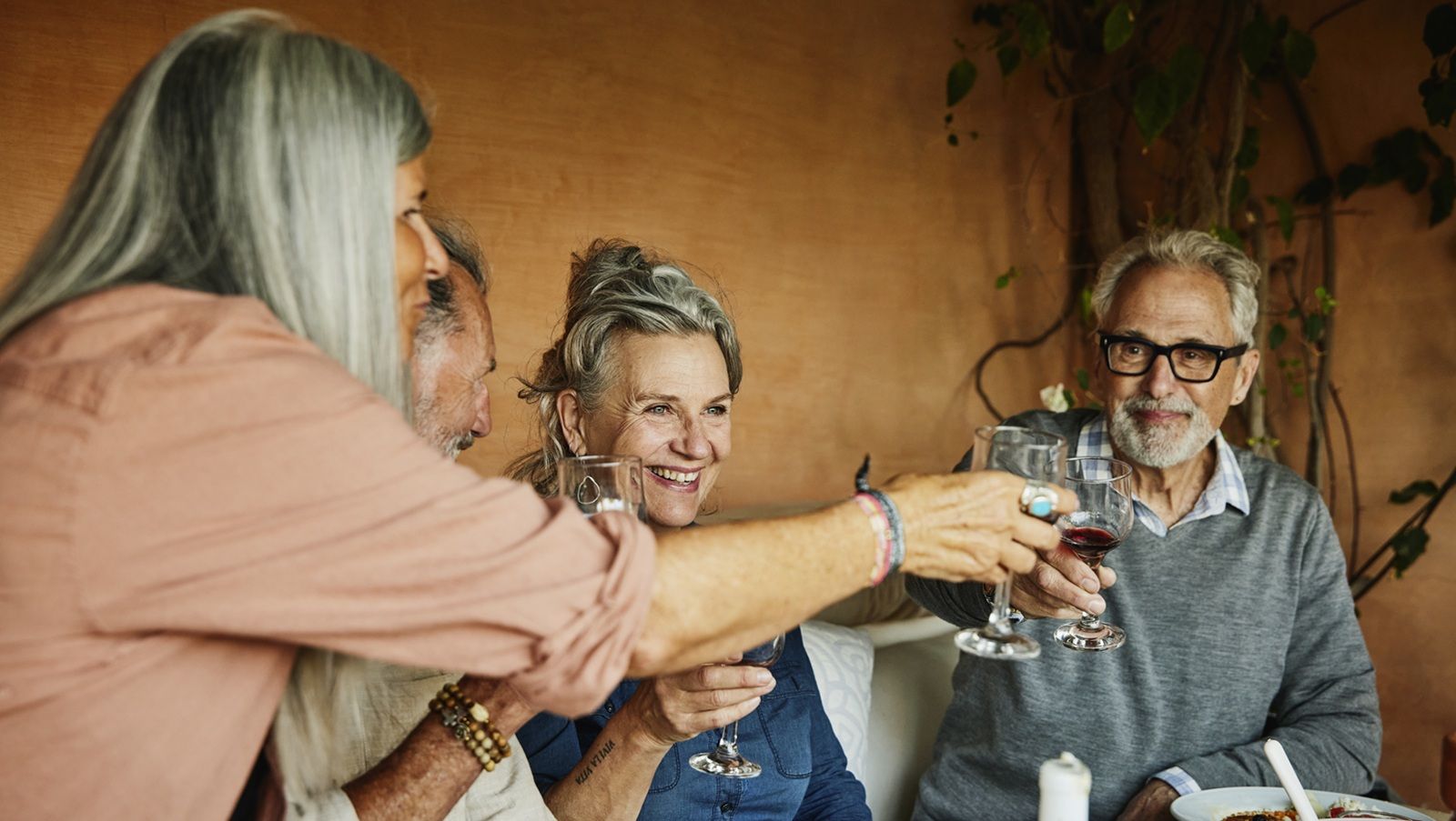 Medium shot of smiling senior friends toasting with wine glasses while sharing dinner at outdoor table at villa during vacation