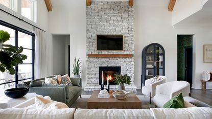 neutral living room with cream sofa and chairs and exposed brick wall with fireplace