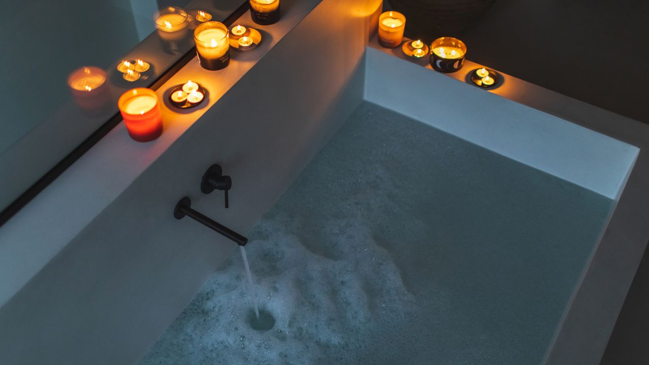 Aerial view of a rectangular bath filling with water and bubbles surrounded by candles in the top left corner