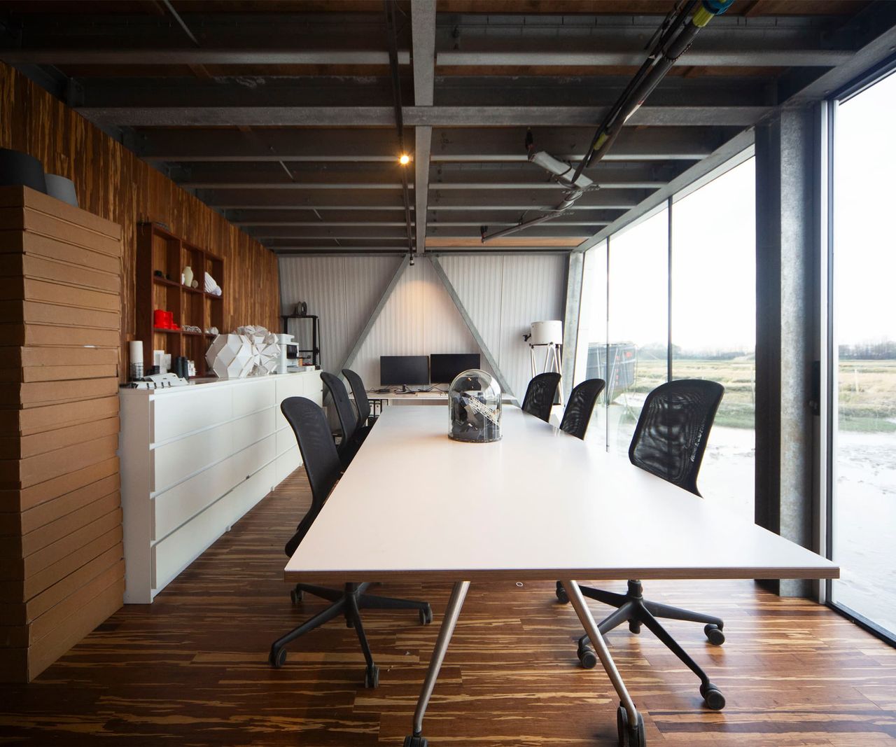 An office room with a glass wall looking onto the sea with steel beams