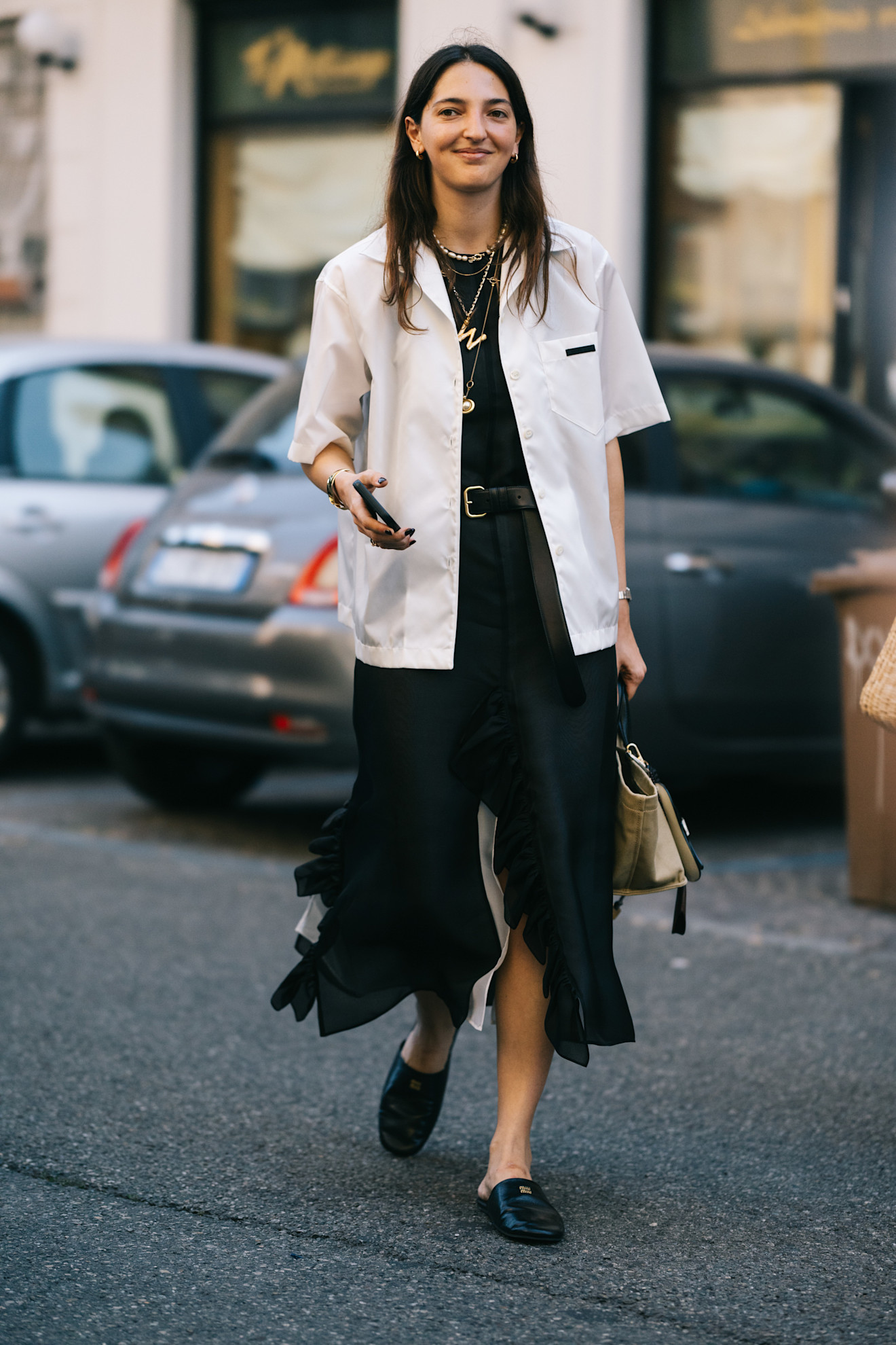 Mens Fashion Week SS26 showgoer wears a white short sleeve shirt over a black top with a black pleated skirt and square-toe black mules.