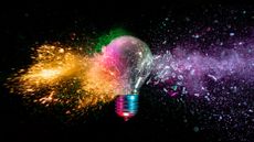 A lightbulb is shattered with various colors coming out of it against a black background