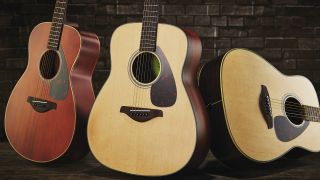 Three Yamaha acoustic guitars leaning against a brick wall