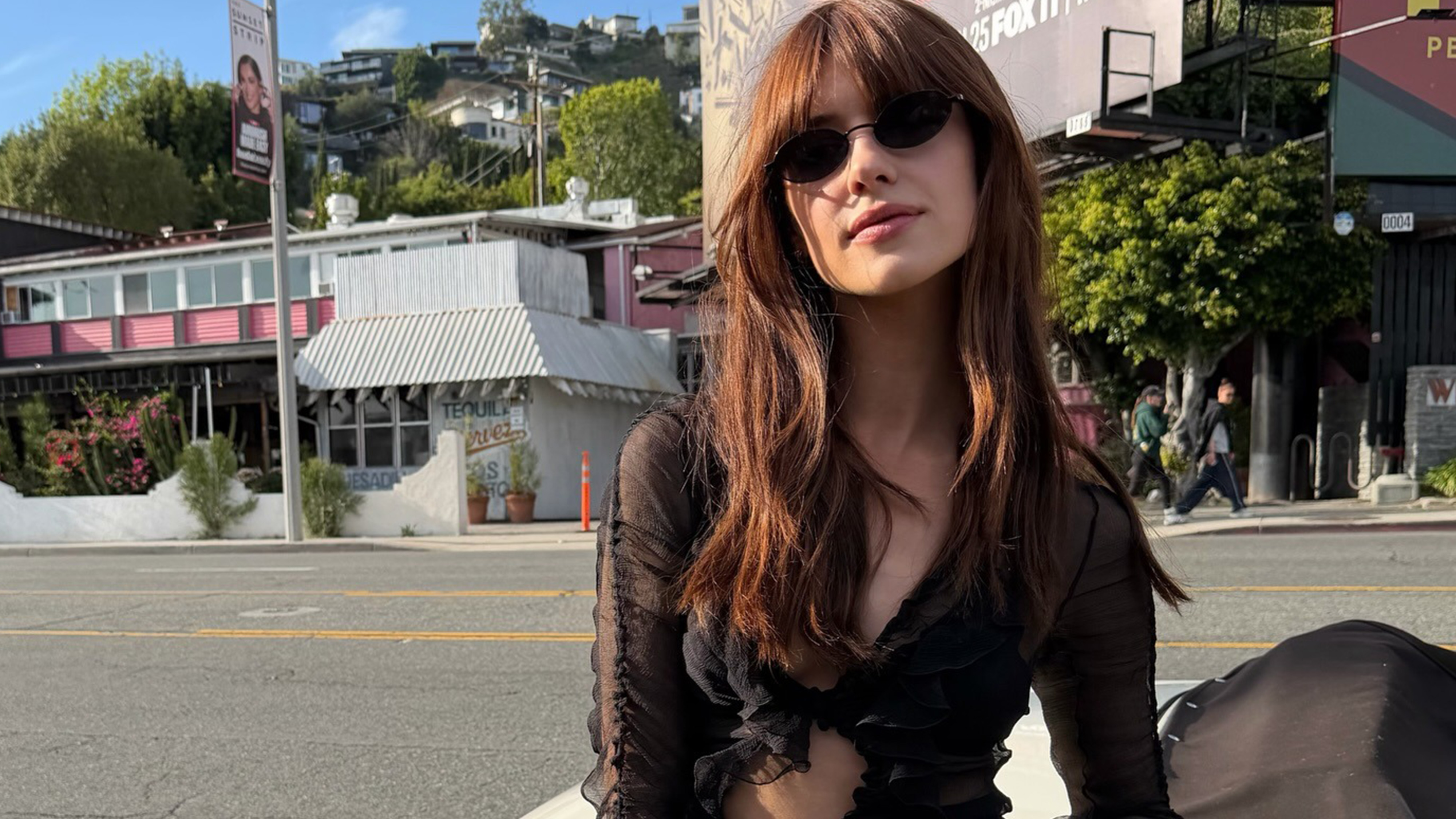 Daisy Edgar-Jones wearing a black going-out top with high-waisted jeans and a black Prada clasp bag on Sunset Boulevard in Los Angeles.