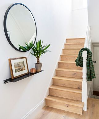 A wooden staircase with round mirror and picture ledge
