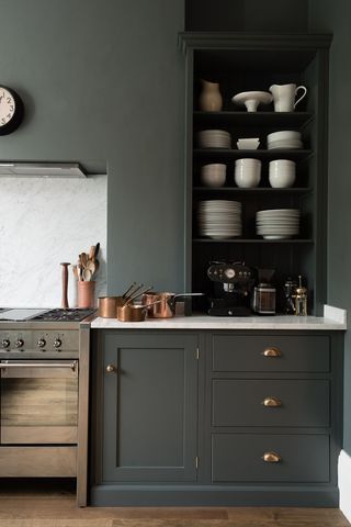 A small kitchen in dark charcoal grey with gold accent and matching colored wall with open cabinetry and stainless steel range cooker