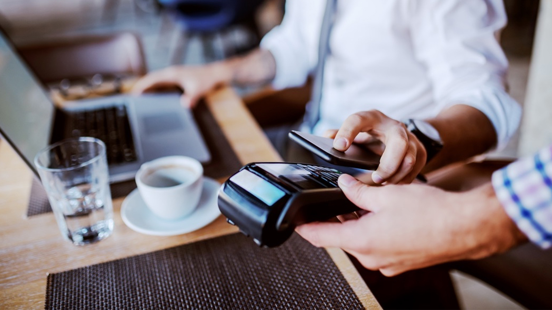 A man is paying for coffee using his phone while another person holds a point of sale terminal for him