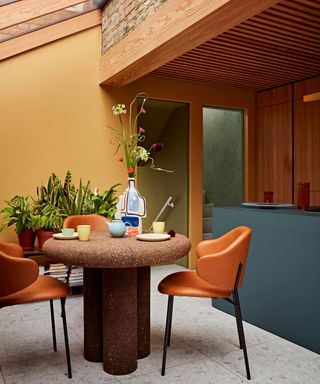 colour block kitchen dining with yellow wall, green kitchen island, cork dining table and leather chairs