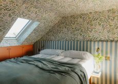 converted loft with floral wallpaper and bed with stripy headboard