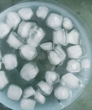 A blue bowl with water and white ice cubes on it, stood on top of a gray surface