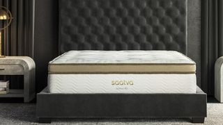 The Saatva HD, Saatva's best mattress for heavier bodies, is shown on a black platform base with a very tall button-tuck black headboard set against a black wall