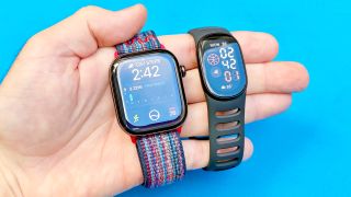 Close-up of both the Apple Watch 12 and Fitbit Edge in a user's hand against a colorful background