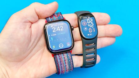 Close-up of both the Apple Watch 12 and Fitbit Edge in a user's hand against a colorful background
